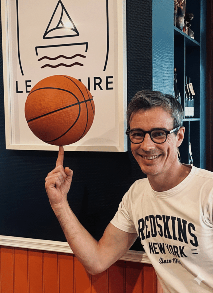 Guillaume, gérant de la Crêperie Le Nazaire à Saint-Nazaire, fait tourner un ballon de basket sur son doigt devant le logo du restaurant, pour célébrer le partenariat avec le club des Fréchets.
